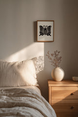 Agehachō butterfly kamon print in black on cream, framed above a wooden nightstand beside the bed in a calm bedroom nook