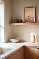 Crane at Dawn print framed on the wall above a wood shelf in a warm ivory kitchen corner