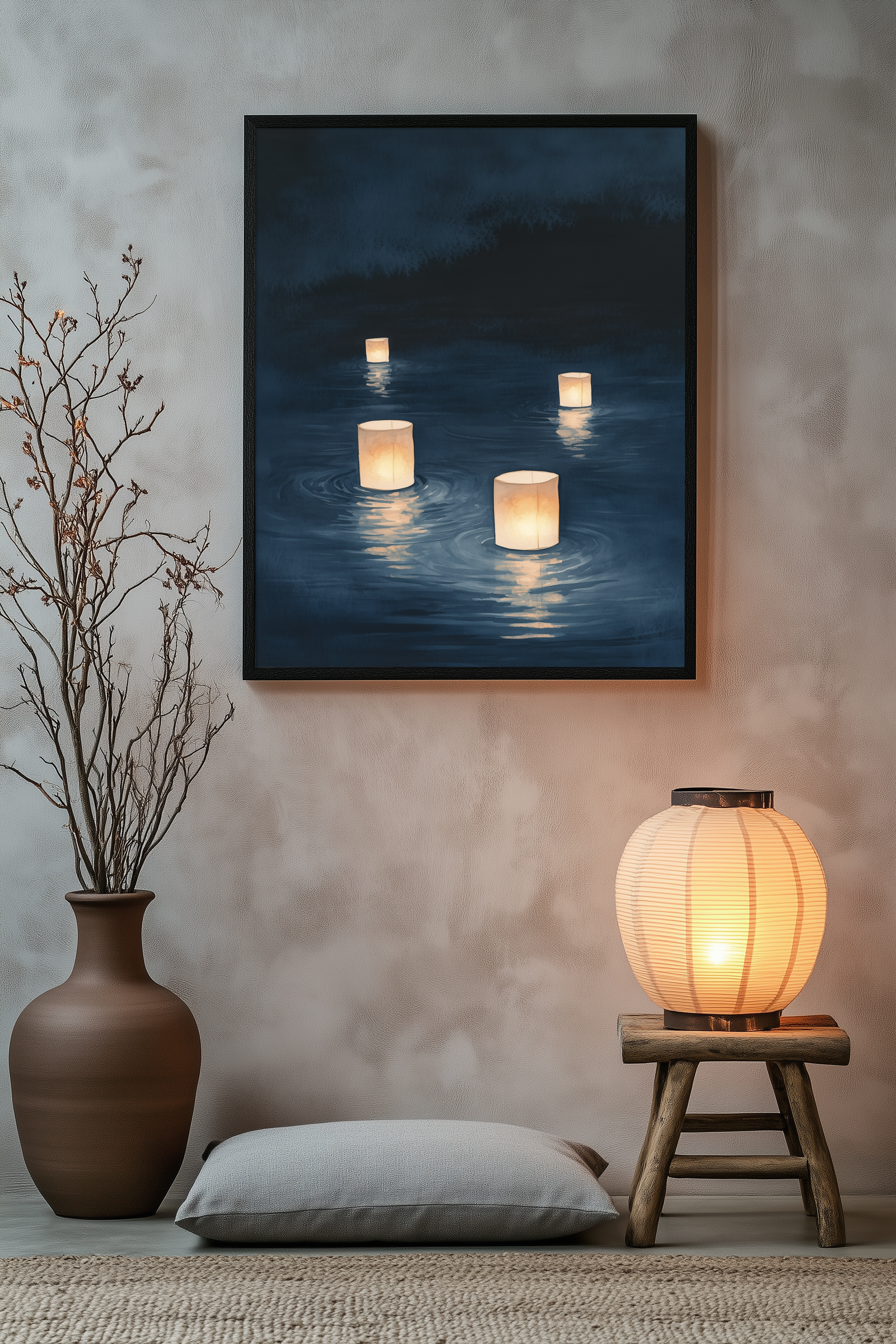 Sumi-e style indigo ink print of paper lanterns floating on dark water, black frame above a floor cushion beside a glowing paper lantern on a wooden stool, Yugen Print