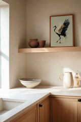 Golden Crane Rising print shown framed in a kitchen corner, a red-crowned crane steps forward with wings spread, black feathers splashing ink and gold seams through its white wing