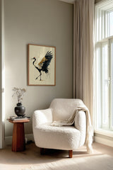 Golden Crane Rising print shown framed in a reading corner, a red-crowned crane steps forward with wings spread, black feathers splashing ink and gold seams through its white wing
