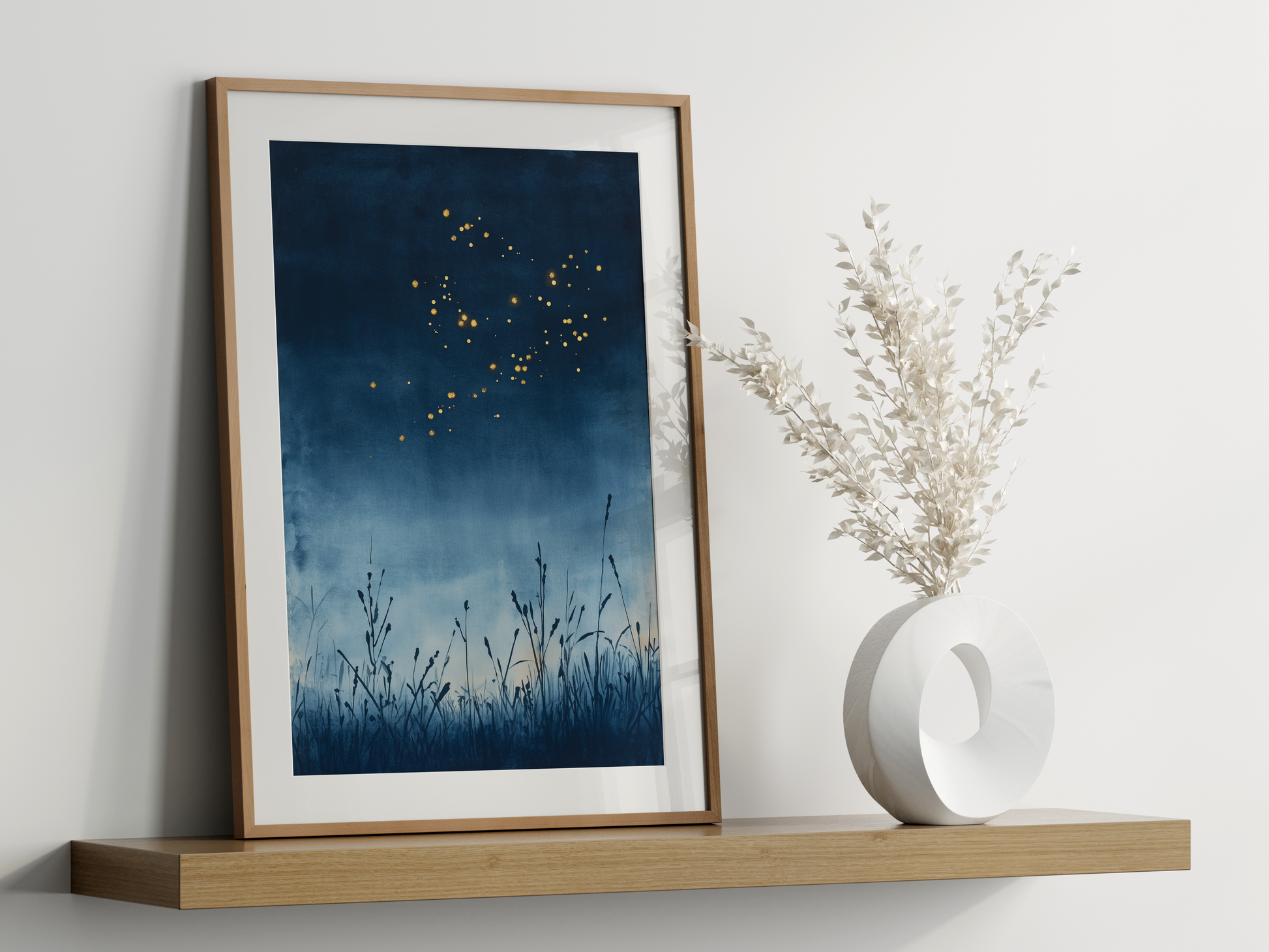 Sumi-e style indigo ink print of golden fireflies over night reeds, oak frame leaning on a floating wood shelf beside a white ceramic vase, Yugen Print