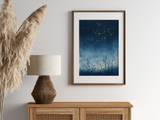Sumi-e style indigo ink print of fireflies drifting over a summer night, oak frame above a rattan sideboard with a woven lamp and dried pampas grass, Yugen Print