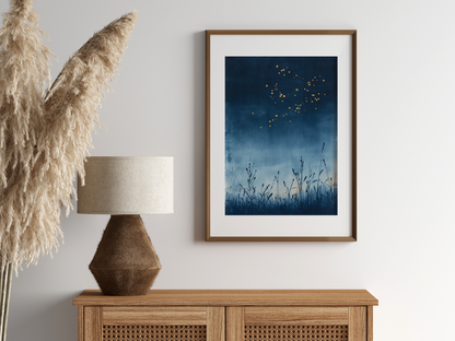 Sumi-e style indigo ink print of fireflies drifting over a summer night, oak frame above a rattan sideboard with a woven lamp and dried pampas grass, Yugen Print