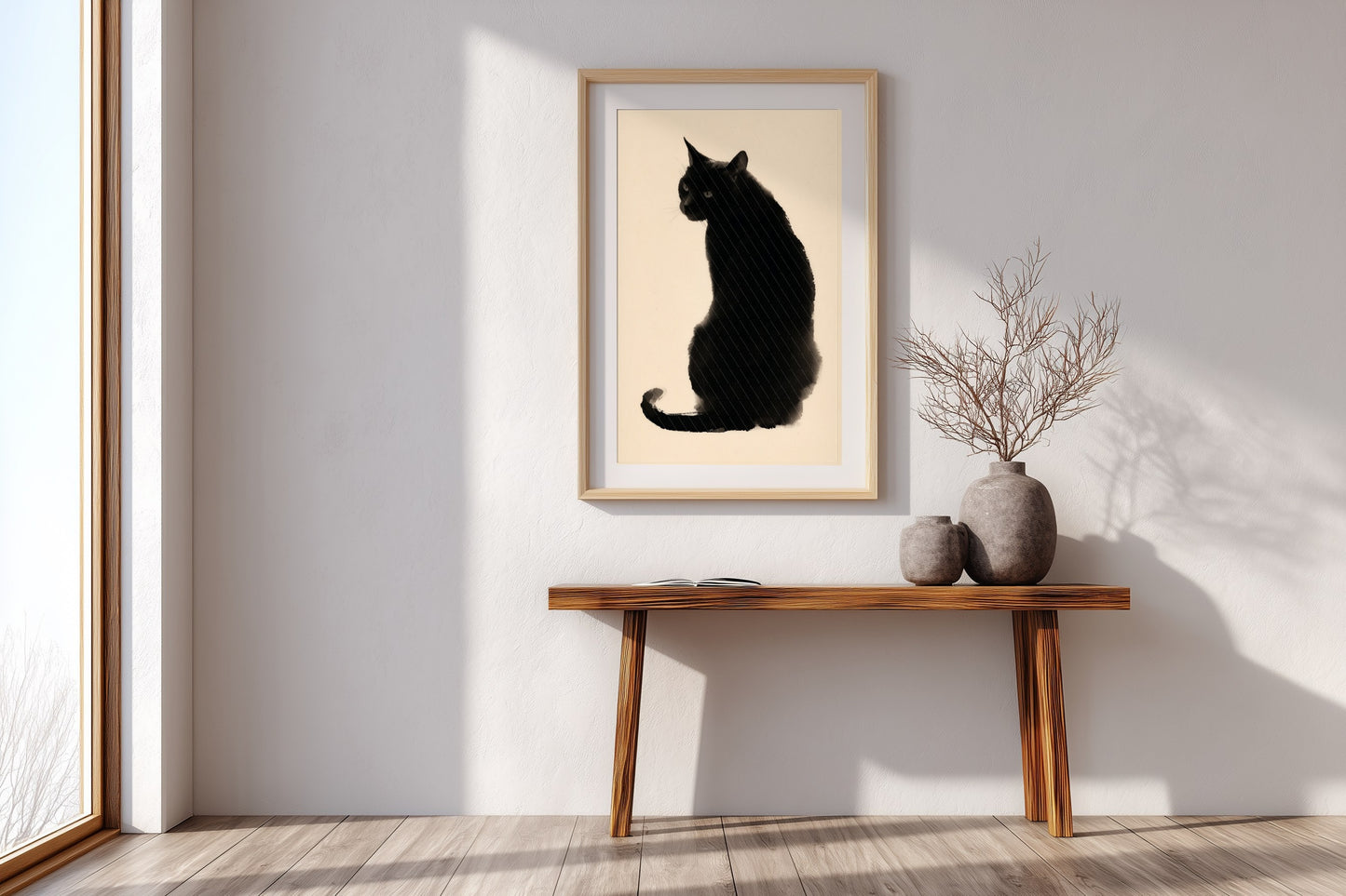 A framed art print of a black cat silhouette on a cream background, displayed on a white wall above a wooden console table with decorative vases in a bright, modern room.