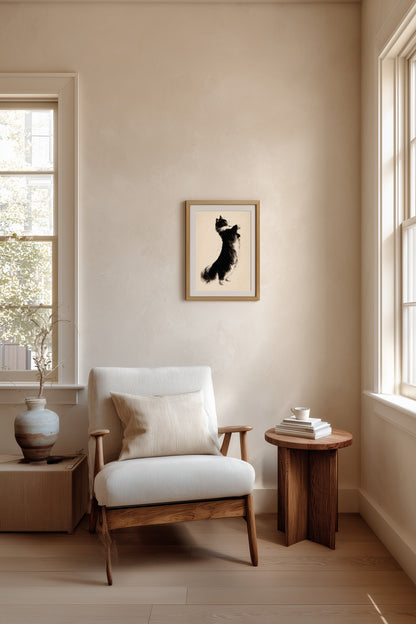 A framed cat silhouette art print hangs on a beige wall in a modern, sunlit room with a white armchair, wooden side table, and light wood floors.