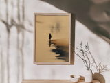 Sumi-e style ink wash print of a lone figure standing at the water's edge with a faint reflection in mist, framed in light wood on an entryway console with a dried branch and ceramic bowls, Yugen Print