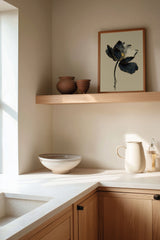 Kintsugi Lotus print shown framed in a kitchen corner, a dark ink lotus flower with gold-edged petals on a curved stem above rippling water