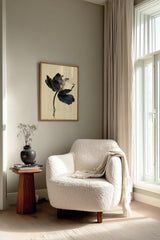 Kintsugi Lotus print shown framed in a reading corner, a dark ink lotus flower with gold-edged petals on a curved stem above rippling water