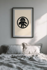Matsu pine kamon print in black on cream, framed above the bed in a calm bedroom with grey linen bedding