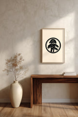 Matsu pine kamon print in black on cream, framed above a dark wood console table with a vase of dried branches
