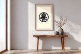 Matsu pine kamon print in black on cream, in a tall frame above a slim wooden console in a minimalist entryway