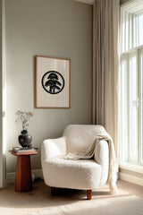 Matsu pine kamon print in black on cream, framed above a cream reading chair by a sunlit window