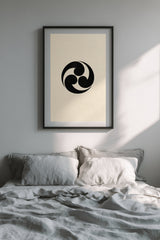 Mitsudomoe swirl kamon print in black on cream, framed above the bed in a calm bedroom with grey linen bedding