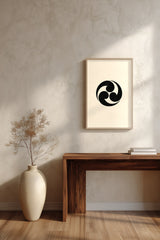 Mitsudomoe swirl kamon print in black on cream, framed above a dark wood console table with a vase of dried branches