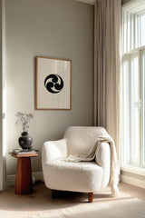 Mitsudomoe swirl kamon print in black on cream, framed above a cream reading chair by a sunlit window