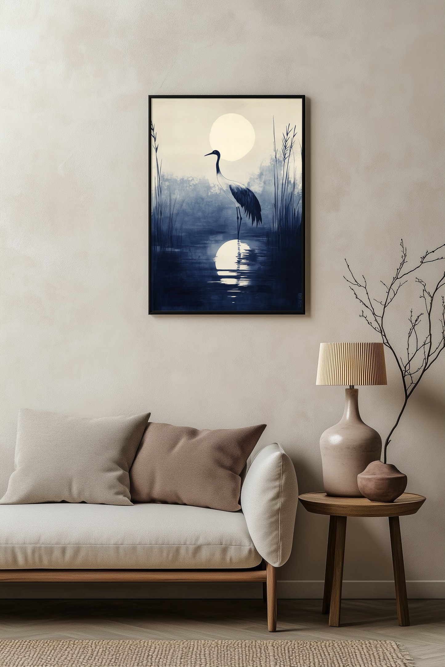 Sumi-e style indigo ink print of a crane silhouetted beneath a full moon, black frame above a pale linen sofa with a wooden side table and ceramic lamp, Yugen Print