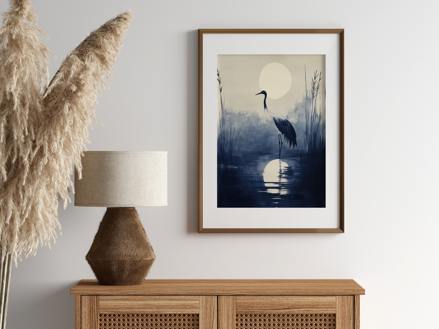Sumi-e style indigo ink print of a crane silhouetted beneath a full moon, oak frame above a rattan sideboard with a woven lamp and dried pampas grass, Yugen Print