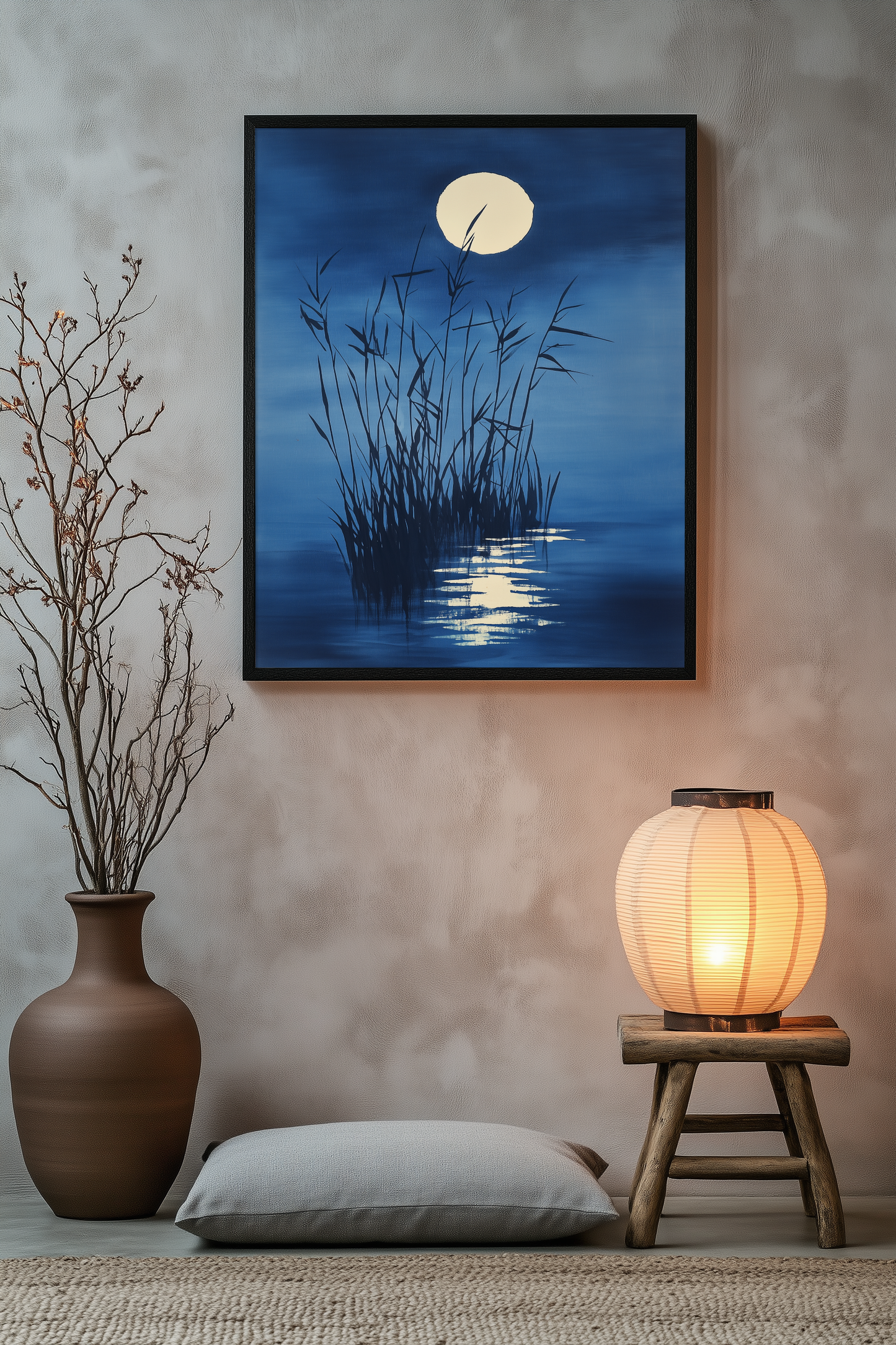 Sumi-e style indigo ink print of tall reeds beneath a full moon, black frame above a floor cushion beside a glowing paper lantern on a wooden stool, Yugen Print