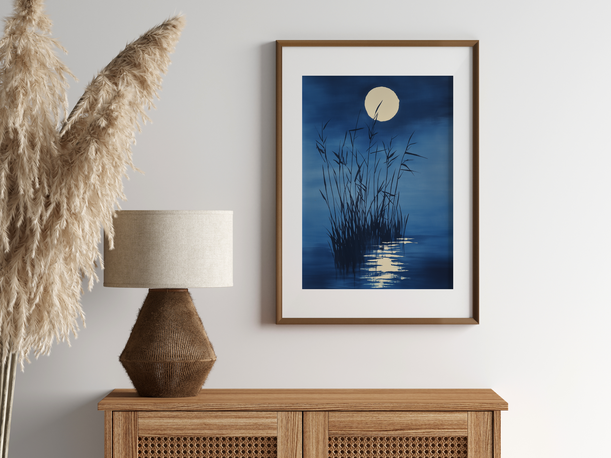 Sumi-e style indigo ink print of moonlit reeds and a full moon reflection, oak frame above a rattan sideboard with a woven lamp and dried pampas grass, Yugen Print
