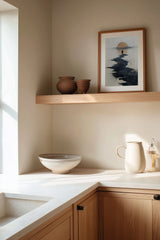 Path to the Setting Sun sumi-e print framed on the wall above a wood shelf in a warm ivory kitchen corner
