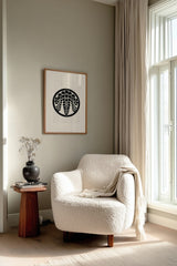 Sagari-fuji wisteria kamon print in black on cream, framed above a cream reading chair by a sunlit window