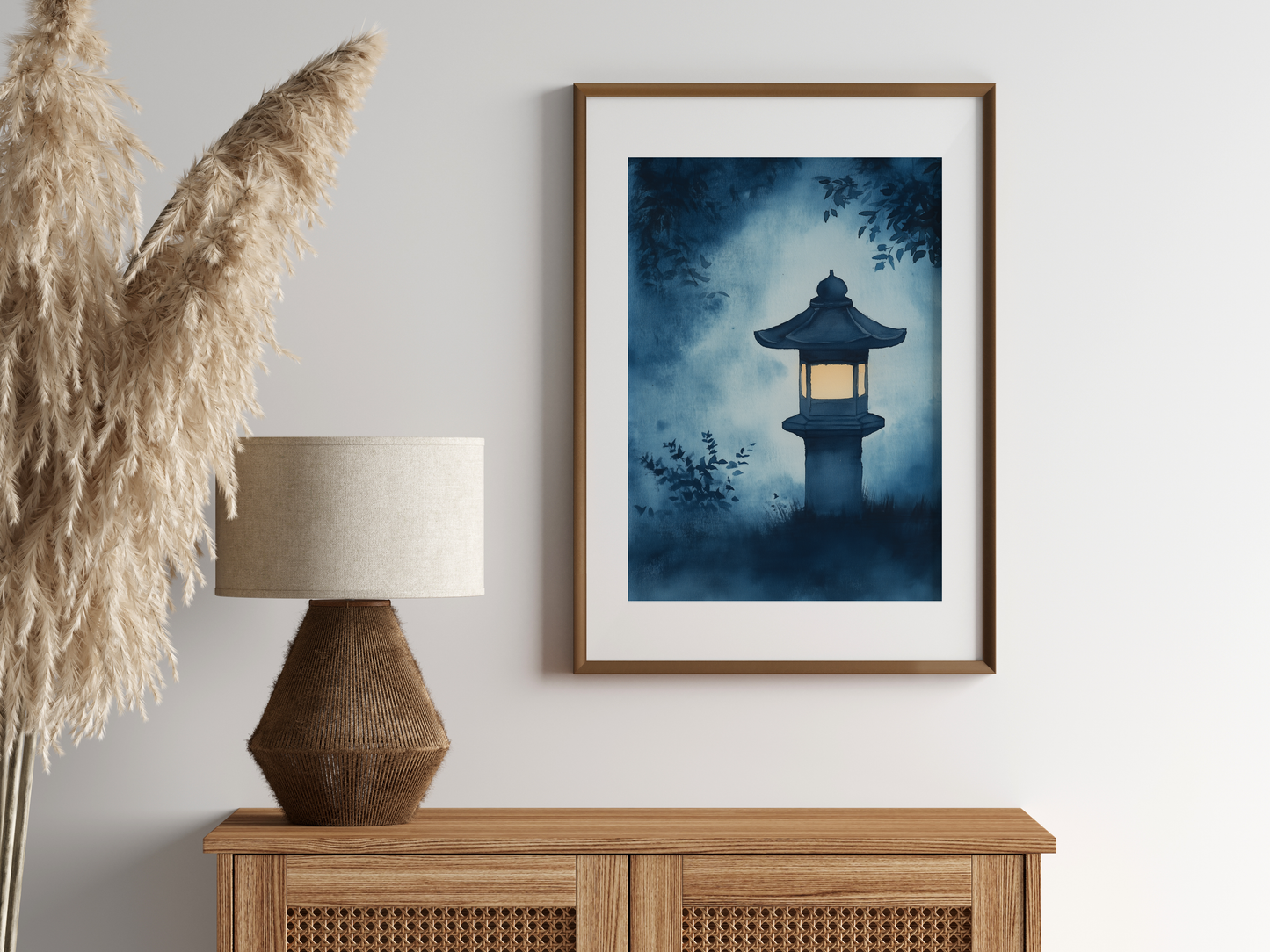 Sumi-e style indigo ink print of a glowing Japanese stone lantern at night, oak frame above a rattan sideboard with a woven lamp and dried pampas grass, Yugen Print