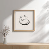Maru sleeping cat print in a square wood frame above a sideboard with a vase of branches, Yugen Print