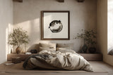 A framed black and white fugu ensō ink art print hangs above a low platform bed with neutral linen bedding, flanked by dried branches and ceramic vases in a serene, sunlit bedroom.