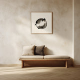 A framed black and white fugu ensō ink art print hangs on a warm cream plaster wall above a low wooden daybed with linen and charcoal cushions in a calm, sunlit minimalist room.
