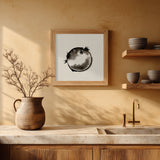 A framed black and white fugu ensō ink art print hangs on a warm ochre kitchen wall above a stone counter, beside open wood shelves of grey ceramic bowls, a terracotta jug, and a brass tap.