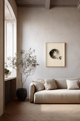 A minimalist living room scene featuring a cream-colored sofa with matching pillows, a large potted dried plant, and a framed black and white fugu art print on the wall.