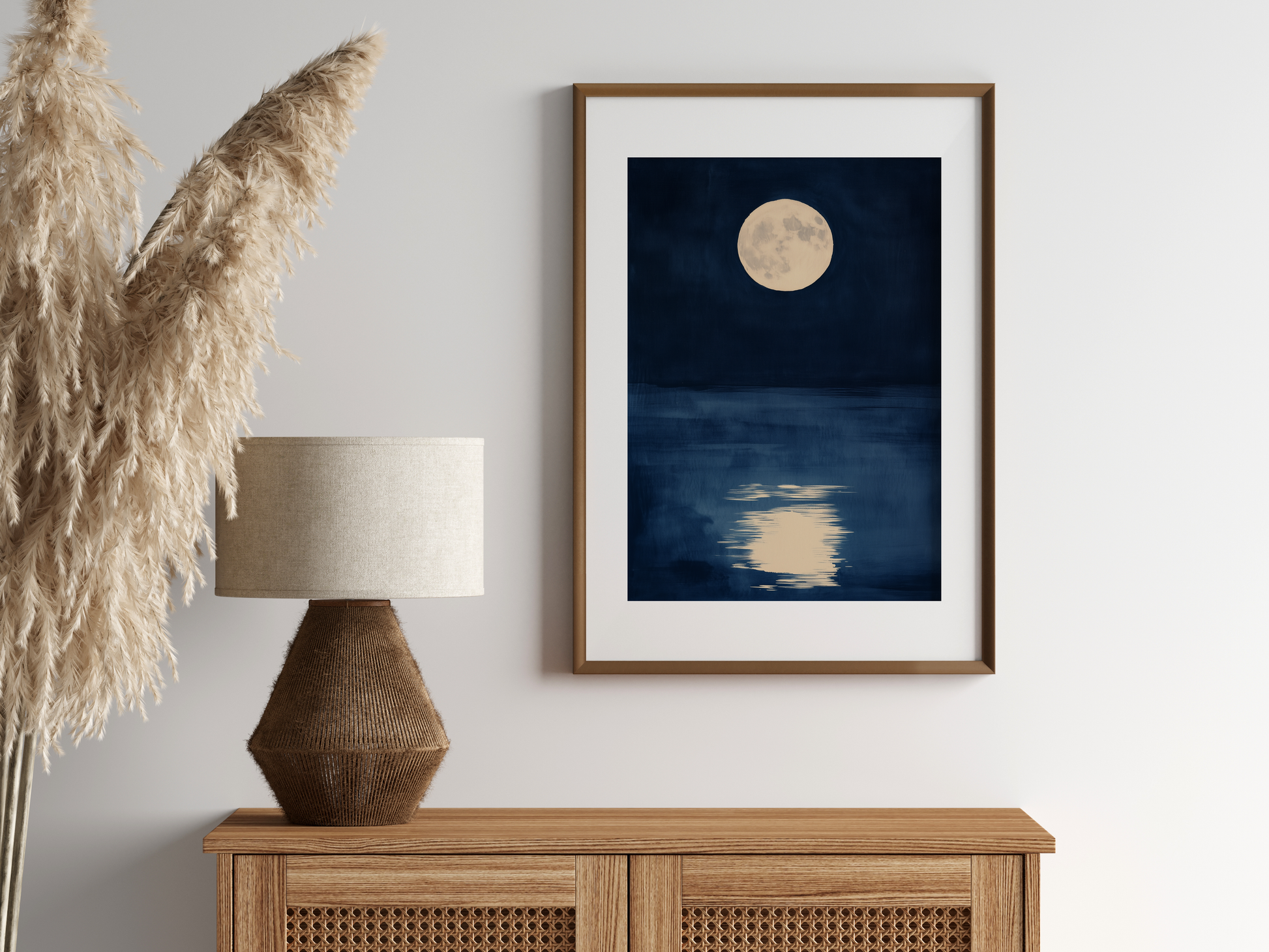 Sumi-e style indigo ink print of a full moon over still water, oak frame above a rattan sideboard with a woven lamp and dried pampas grass, Yugen Print