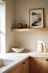 The Amber Shore sumi-e print framed on the wall above a wood shelf in a warm ivory kitchen corner