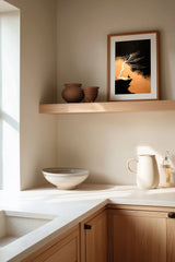 The Cliff Tree sumi-e print framed on the wall above a wood shelf in a warm ivory kitchen corner