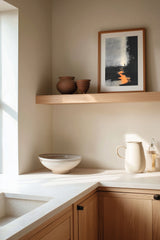 The Ember Stair sumi-e print framed on the wall above a wood shelf in a warm ivory kitchen corner