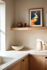 The Golden River sumi-e print framed on the wall above a wood shelf in a warm ivory kitchen corner