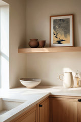 The White Tree sumi-e print framed on the wall above a wood shelf in a warm ivory kitchen corner
