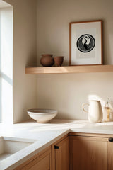 Tsuru crane kamon print in black on cream, framed on a wooden kitchen shelf with stoneware ceramics