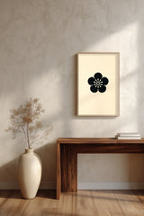 Ume plum blossom kamon print in black on cream, framed above a dark wood console table with a vase of dried branches