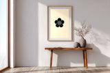 Ume plum blossom kamon print in black on cream, in a tall frame above a slim wooden console in a minimalist entryway