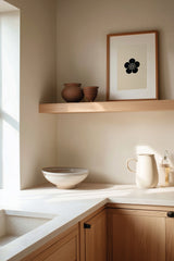 Ume plum blossom kamon print in black on cream, framed on a wooden kitchen shelf with stoneware ceramics