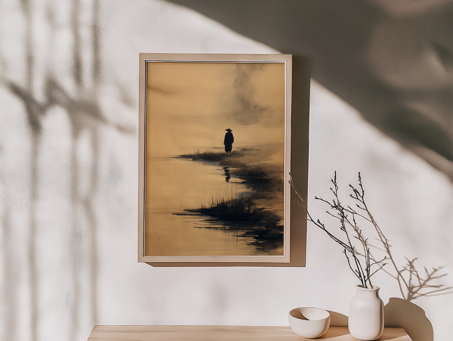 Sumi-e style ink print of a lone figure walking a misty shoreline with a soft reflection in the water, framed in light wood on an entryway console with a dried branch and ceramic bowls, Yugen Print